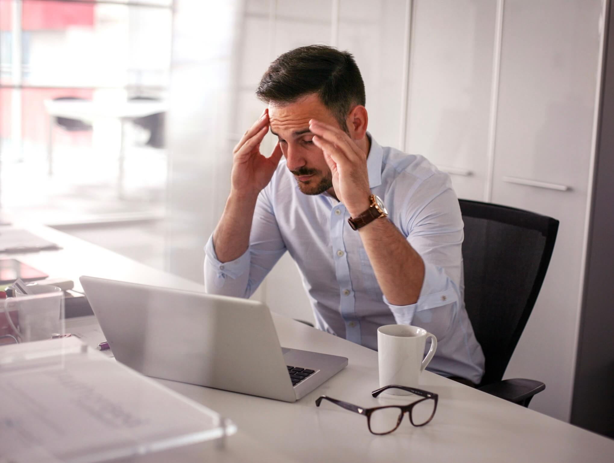 パソコン仕事で目が疲れて頭を抱えている人の写真