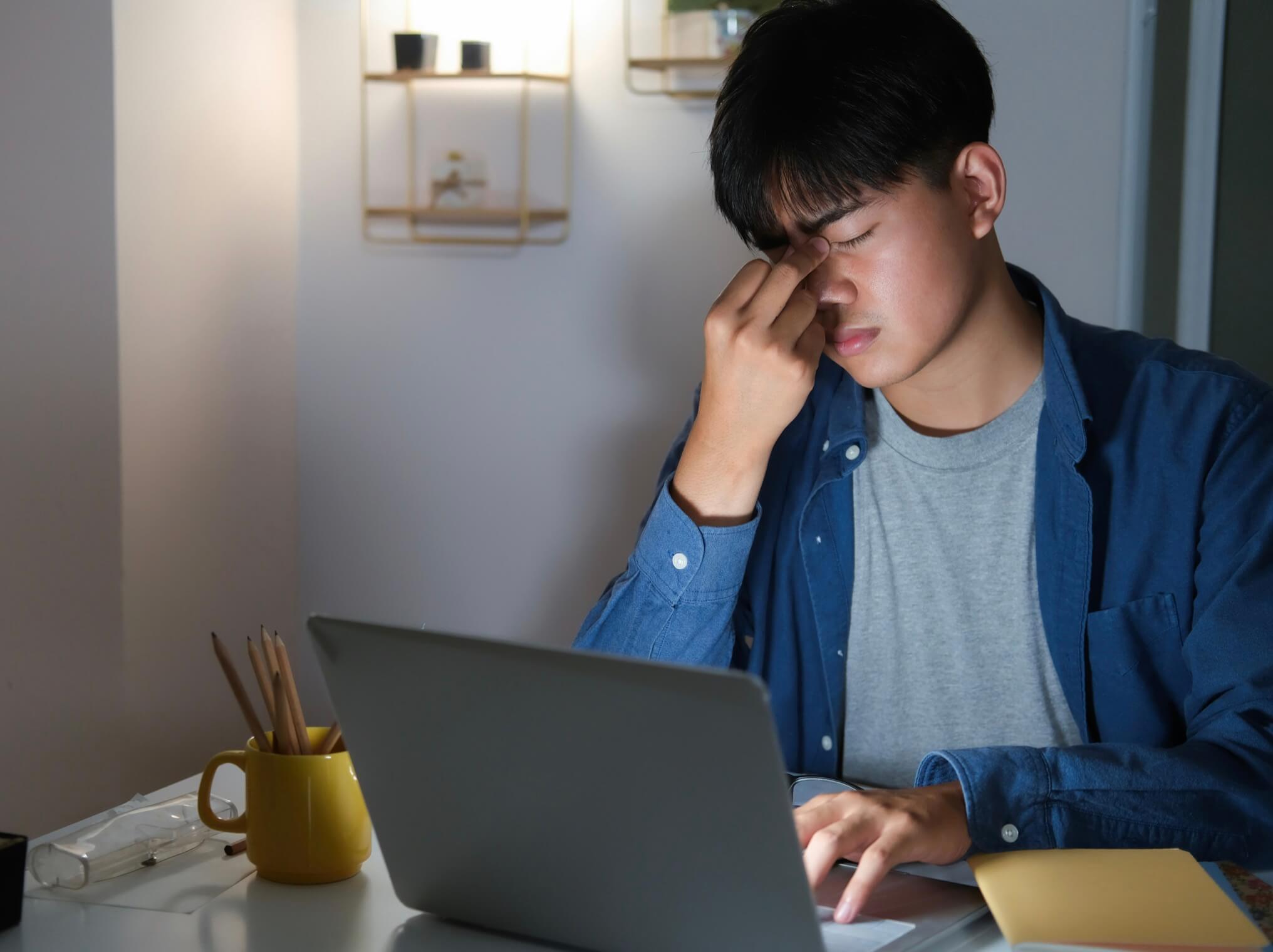 仕事中にパソコンの前で目が疲れて目をおさえている人の写真