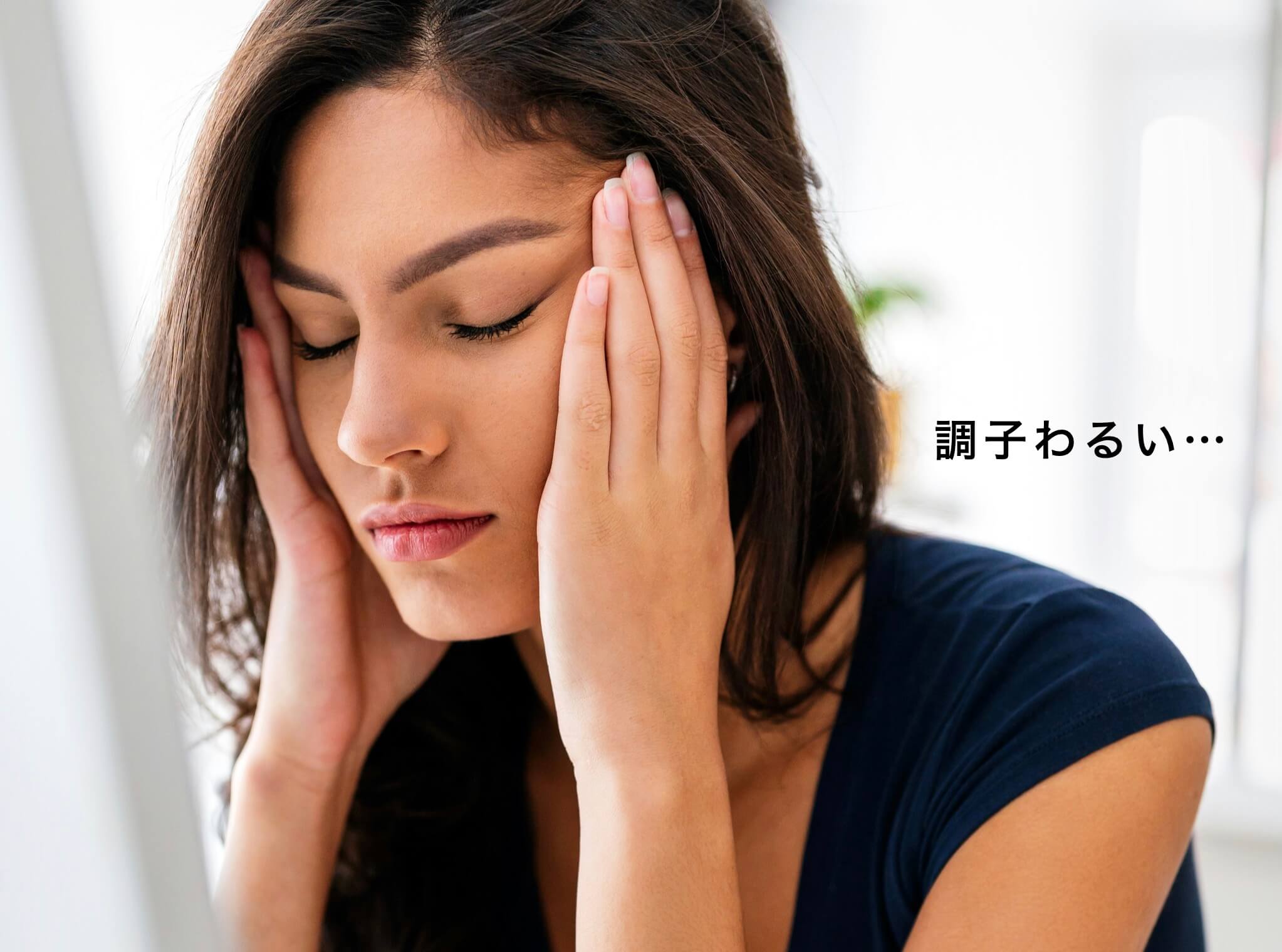 調子がわるく目頭をおさえてしんどそうな女性の写真