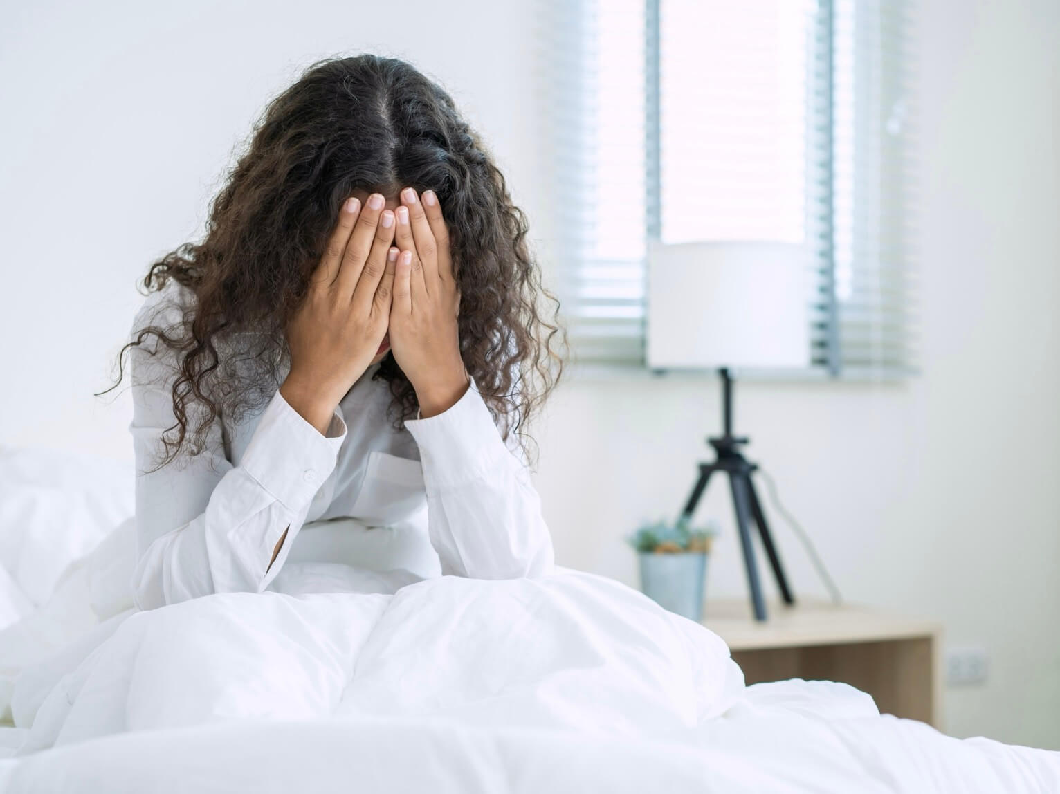 貧血の症状で眩まいがしてベッドからなかなか起き上がれない女性の写真