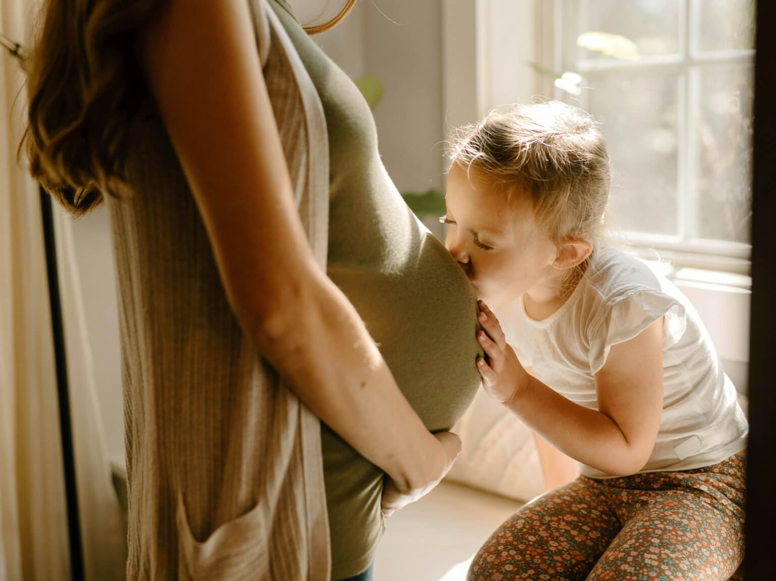 ヘム鉄サプリを飲みながら妊娠中を過ごす母親とそのお腹にキスりする子供の写真